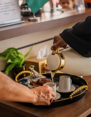 Arabic coffee being poured from a dallah into cups on a tray